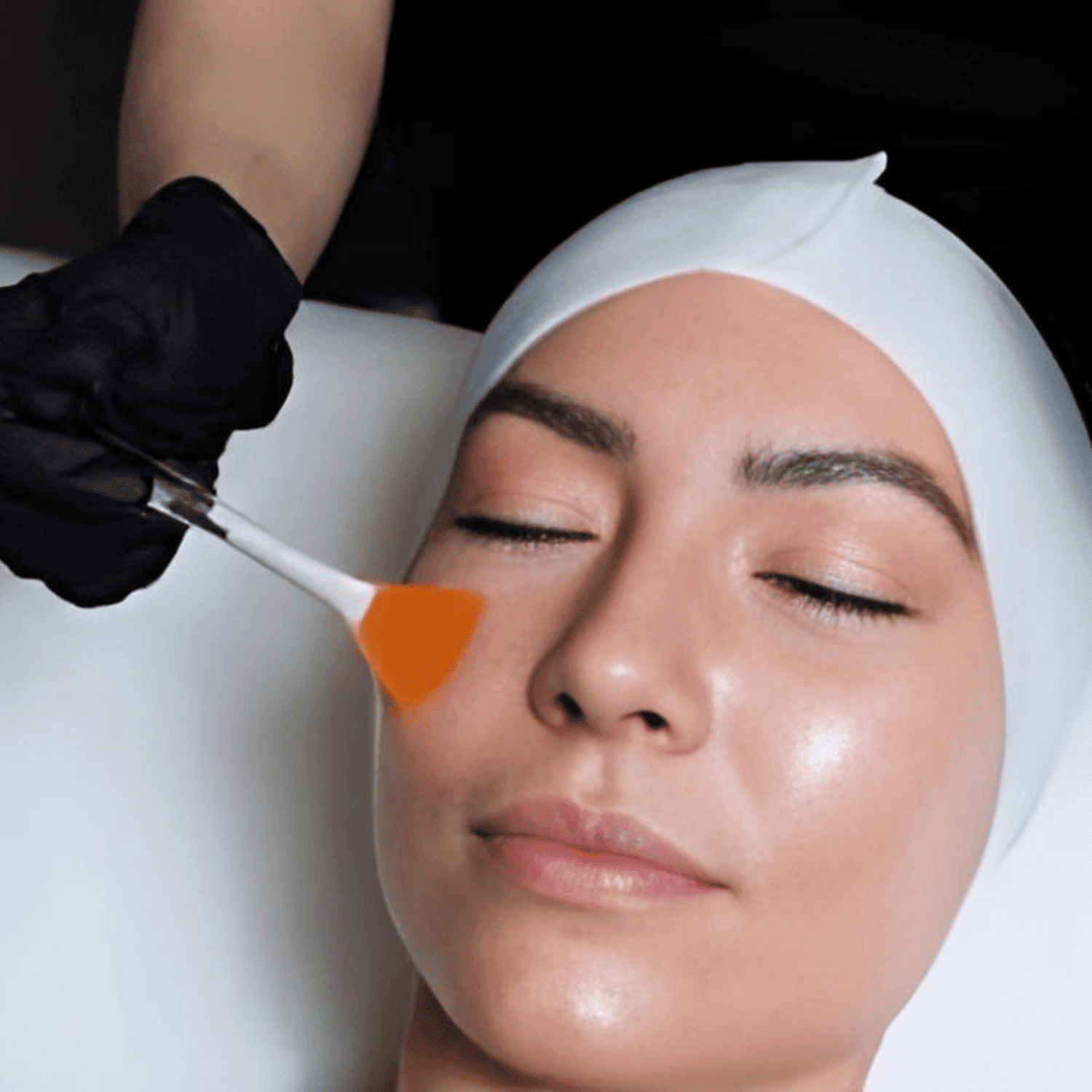 Facial treatment: person receiving a brush-applied face mask by an esthetician.