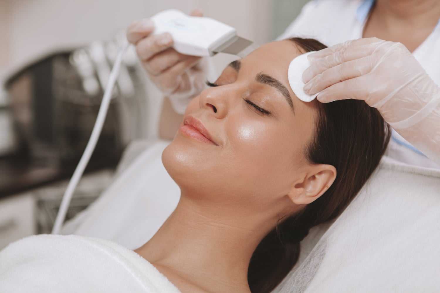 Woman receiving a facial treatment from a professional with skincare equipment.