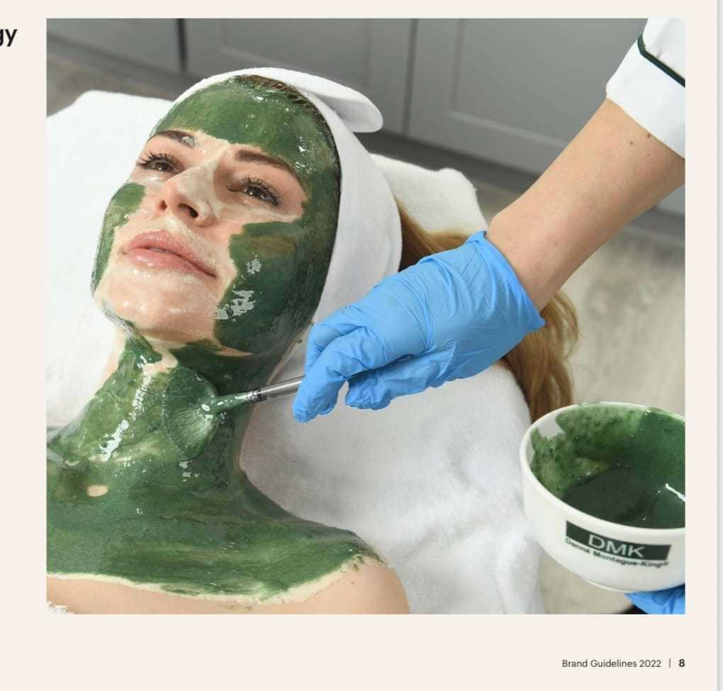 Person receiving a green facial mask treatment at a spa, with a gloved hand applying the mask.