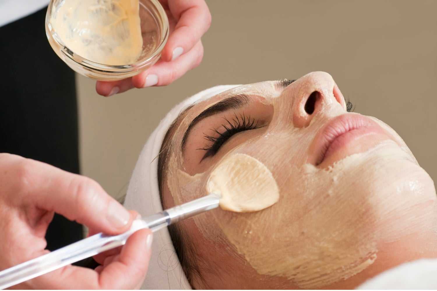 Facial treatment applied with a brush while woman relaxes in a spa.